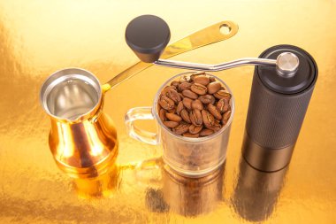 Sade bir kahve öğütücüsünün yakın çekimi, parlak bir bakır çakmak, ve kahve çekirdekli cam bardak, kahve hazırlama görselleri için temiz altın zemin üzerine kurulmuş.