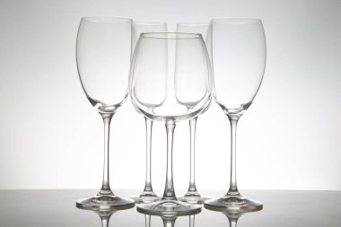 Uzun sapları ve temiz kâseleri olan zarif şarap kadehleri, parlak bir yüzeyde yansımaları olan, lüks yemek ve kutlama temaları için mükemmel bir sırada dizilmiş..