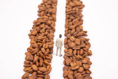 Kahve çekirdekleri arasındaki takım elbiseli küçük bir şahsın metaforik portresi kahve işindeki kararlılığı temsil ediyor. Beyaz arkaplan.