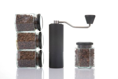 Kahve çekirdekleri için siyah manuel kahve öğütücüsü ve siyah kahve çekirdekleri ile dolu dört cam şeffaf kavanoz ve beyaz arka planda kahve demlemek için toprak takımı. Kahve için mutfak aletleri..