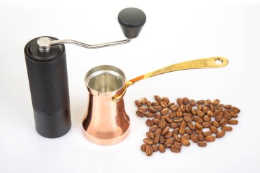 Metalik saplı siyah bir el yapımı kahve öğütücüsü, bakır bir çakmak taşının ve beyaz arka planda kızarmış kahve çekirdeklerinin yanında oturur. Kahve demlemek için birebirdir..