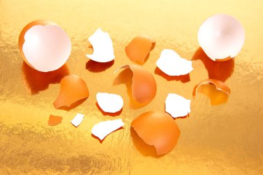 Parlak altın bir arka planda dağınık kabuklu kırık yumurtalar minimalist ve dokulu bir mutfak yaşamında sıcak, lüks bir tonu yansıtıyor.