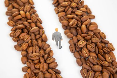 Kahve çekirdekleri arasında yürüyen takım elbiseli küçük bir heykelciğin yer aldığı eşsiz stok fotoğrafı kahve pazarındaki bir iş yolunu gösteriyor.