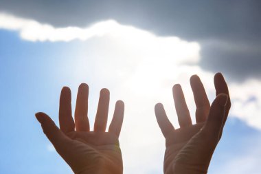 Siluet parlak bir güneşe ve bulutlu gökyüzüne karşı el kaldırdı, doğadaki özgürlüğü, umudu ve ruhsal bağlantıyı simgeliyor..