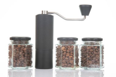 Kahve çekirdekleri için siyah manuel kahve öğütücüsü ve siyah kahve çekirdekleri ile dolu üç bardak şeffaf kavanoz ve beyaz arka planda kahve demlemek için toprak takımı. Kahve için mutfak aletleri..