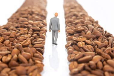 Kahve çekirdekleri arasında yol alan takım elbiseli minicik bir figürün kavramsal görüntüsü kahve ticareti kariyerini simgeliyor.