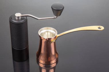 Altın saplı geleneksel bakır bir kahve öğütücüsüyle eşleştirilmiş, kahve meraklıları için koyu bir arka planda sergilenen modern siyah bir el değirmeni..