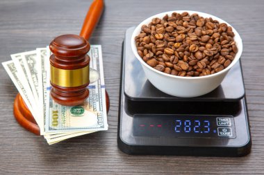 282.3 gramlık dijital ölçek, bir kase kahve çekirdeği ağırlığında. Tahta bir tokmak ve 100 dolarlık banknotlar (100 dolarlık banknotlar da dahil) adalet veya ticareti sembolize eden koyu bir ahşap yüzeye yerleştirilir. Kahve ticareti yasası