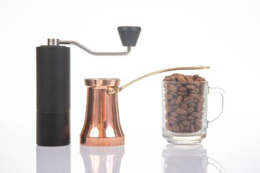 Siyah manuel kahve öğütücüsü, altın saplı bakır bir çakmak, ve beyaz arka planda kavrulmuş kahve çekirdekleri ile dolu cam bir bardak, kahve demlemek için mükemmel.