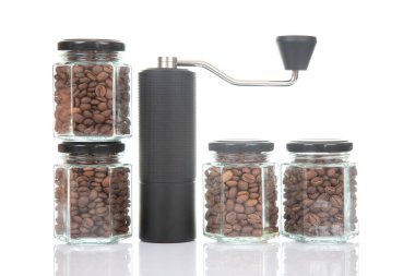 Kahve çekirdekleri için siyah manuel kahve öğütücüsü ve siyah kahve çekirdekleri ile dolu dört cam şeffaf kavanoz ve beyaz arka planda kahve demlemek için toprak takımı. Kahve için mutfak aletleri..