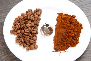 Kavrulmuş kahve çekirdekleri, metal bir öğütücü ve beyaz bir fonda ince bir öğütülmüş kahve. Kahve hazırlama ve gurme görselleri için mükemmel..