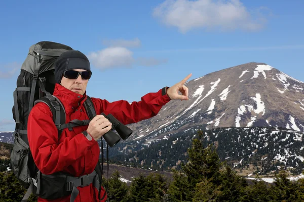 Путешественник с рюкзаком красная куртка с биноклем в руке на склонах точек монтирования на расстояние с пальцем — стоковое фото