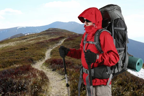Оборудован путешественником в красной куртке стоит на склоне холма — стоковое фото