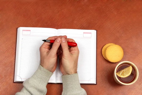 Dos manos con la pluma roja que miente en un cuaderno en escritorio de la oficina — Foto de Stock