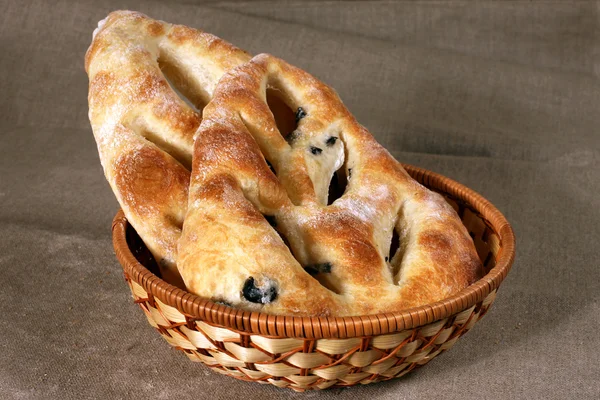 Άσπρο ψωμί γεμισμένο με ελιές βρίσκεται σε ένα ψάθινο καλάθι σε γκρι λινό — Φωτογραφία Αρχείου
