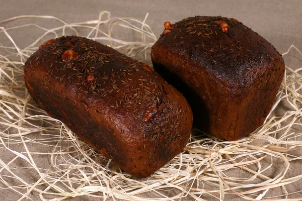 Dos panes oscuros rellenos de queso tirado en paja sobre lino gris — Foto de Stock