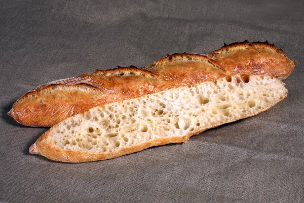 Κόβουν απέναντι τα ψέματα μακρύ άσπρο ψωμί σε μια γκρίζα τραπεζομάντιλο λινού — Φωτογραφία Αρχείου