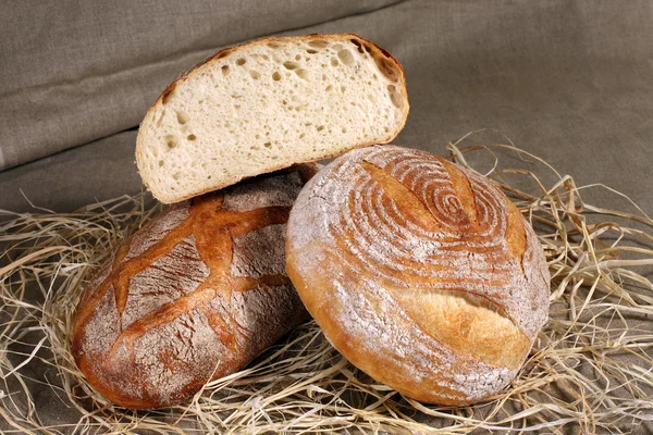 Biały chleb dwa różne formy leżącego w słomy na szary len — Zdjęcie stockowe