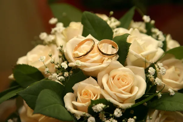 Gold wedding rings lie on a bouquet of roses — Stock Photo, Image