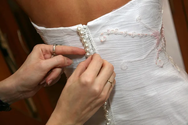 Подружка невесты помогает закрепить пуговицы на платье невесты — стоковое фото