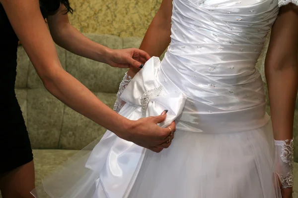 Подружка невесты помогает исправить лук на платье невесты — стоковое фото
