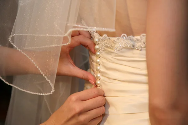 Bridesmaid helps to wear the dress the bride from the back — Stock Photo, Image