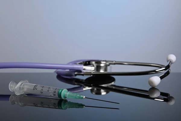 Inoculation Syringe and Medical Stethoscope on a Glass Desk