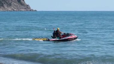 Çocuklu bir adam yazın jet ski ile kıyıdan denize açılır. Denizdeki cazibe ve eğlence. Spor ve eğlence sektörü. Yüksek kalite 4k görüntü