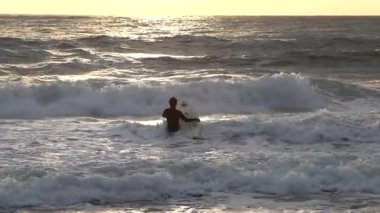 Sıcak dalış kıyafeti giyen sörfçü gün batımında sörf tahtası ile suya girer. İtalya 'da kış sporları. Sağlık, deniz ve doğa. Yüksek kalite 4k görüntü