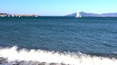 Beyaz yelkenli yelkenli, güneşli bir günde mavi denizde marinadan ayrılıyor. Doğa ve ulaşım. Dinlenme ve turizm. - Evet. Yüksek kalite 4k görüntü