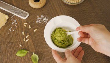 Beyaz kasede taze fesleğen pesto karıştıran biri. Ahşap masada seramik kasede yeşil İtalyan pesto Genovese sosunu karıştıran şefin elleri. Parmesan içerikli yüksek açılı çekim.