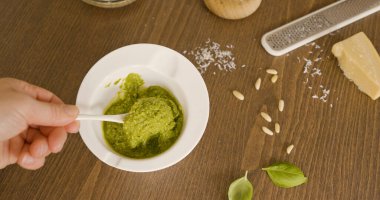 Beyaz kasede taze fesleğen pesto karıştıran biri. Ahşap masada seramik kasede yeşil İtalyan pesto Genovese sosunu karıştıran şefin elleri. Parmesan içerikli yüksek açılı çekim.