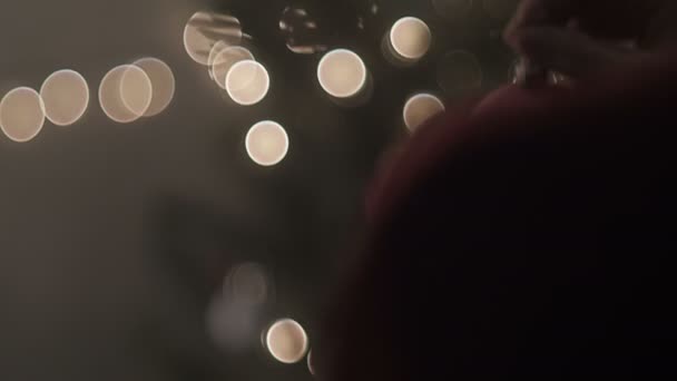 女性のウォーキングは夜にクリスマスツリーを飾るためにクリスマスボールを保持します — ストック動画