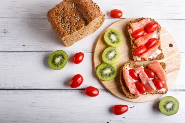 Beyaz ahşap arka planda tereyağlı ve kiraz domatesli füme somon sandviçi. Üst görünüm, boşluk kopyala.