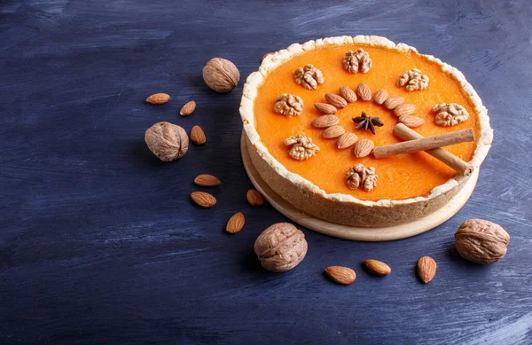 Traditional american sweet pumpkin pie decorated with nuts, on dark blue wooden background. close up.