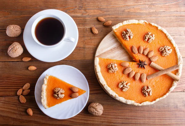 Traditional american sweet pumpkin pie decorated with nuts, on brown wooden background. cup of coffee. top view.