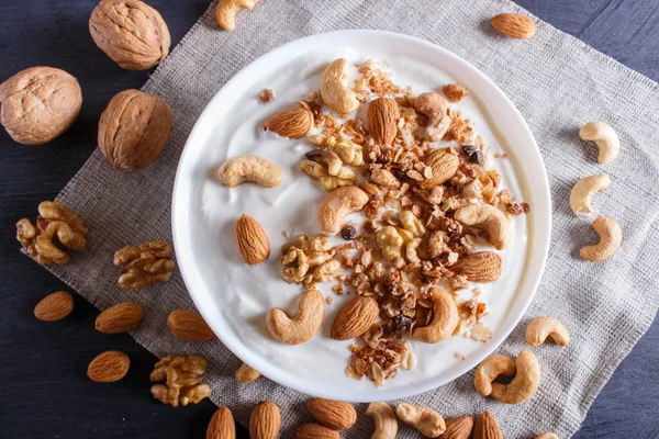 Yunan yoğurtlu beyaz tabak, granola, badem, ceviz, siyah ahşap arka planda ceviz. en üstteki görünüm.