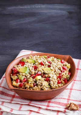 Karabuğday salatası, avokado, ceviz ve nar tohumları siyah ahşap kaplama kil tabakta. Yan görünüm, boşluk kopyala.