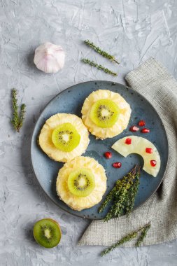 Gri arka planda ananas, peynir ve kivi ile fırında domuz parçaları..