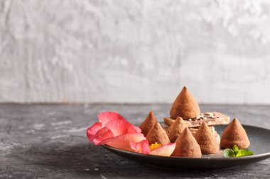 Mavi seramik tabakta çikolatalı trüf. Siyah beton arka planda gül yapraklarıyla süslenmiş. Yaklaş, yan görüş. Boşluğu kopyala.