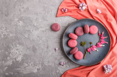 Mor ve pembe badem kurabiyesi veya kanayan kalp çiçekleri ve gri beton arka planda mavi seramik tabakta kırmızı tekstil olan badem kurabiyesi. Düz konum, üst görünüm, kopyalama alanı.