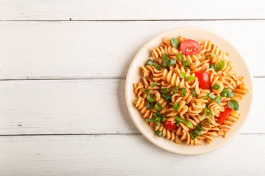 Domates soslu fusilli makarna, beyaz ahşap arka planda kiraz domatesleri, marul ve otlar. Üst görünüm, düz görünüm, kopyalama alanı.