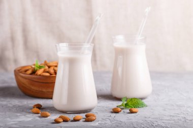 Süt içermeyen organik badem sütü ve gri beton arka planda badem fıstıklı ahşap tabak. Vejetaryen sağlıklı gıda konsepti, yakın plan, yan görüş..