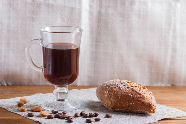Glass cup of coffee with bun on a wooden background and linen textile. close up, copy space.
