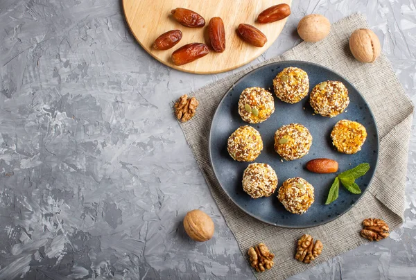 Energy ball cakes with dried apricots, sesame, linen, walnuts and dates with green mint leaves on a blue ceramic plate on a gray concrete  background. linen napkin, top view, copy space, flat lay. vegan homemade candy.