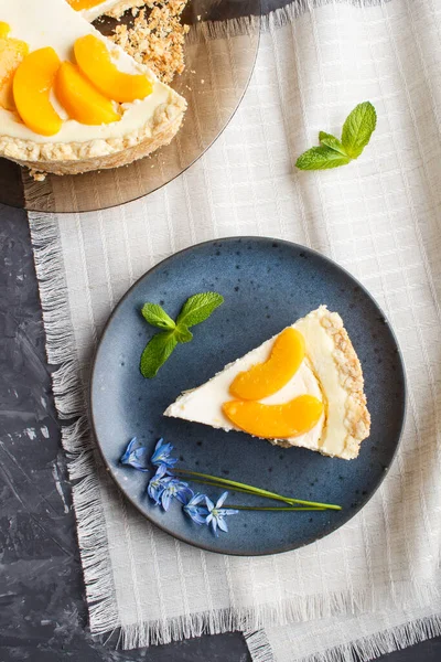 A piece of peach cheesecake on a blue ceramic plate with blue flowers on a linen napkin on a black concrete background. top view, copy space.