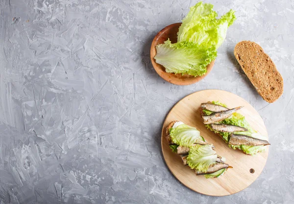 Sprats sandwiches with lettuce and cream cheese on wooden board on a gray concrete background. top view, copy space, flat lay. — Stock Image Sprats Sandwiches Lettuce Cream Cheese Wooden Board Gray Concrete Background Royalty Free Stock Photos