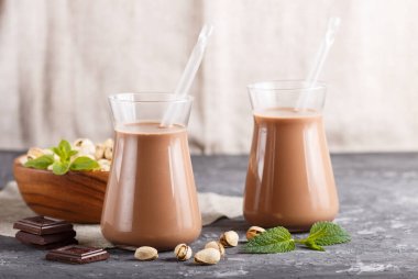 Süt ürünü olmayan organik pistache çikolatalı süt ve gri beton arka planda şam fıstıklı ahşap tabak. Vegan sağlıklı gıda konsepti, yakın çekim, yan görüş, kopyalama alanı.