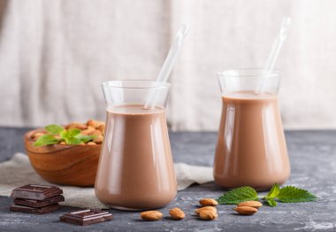 Sütsüz organik badem çikolatalı süt ve siyah beton arka planda badem fıstıklı ahşap tabak. Vejetaryen sağlıklı gıda konsepti, yakın plan, yan görüş..