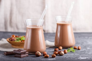 Süt içermeyen organik fındıklı çikolatalı süt ve siyah beton arka planda fındıklı tahta tabak. Vejetaryen sağlıklı gıda konsepti, yakın plan, yan görüş..